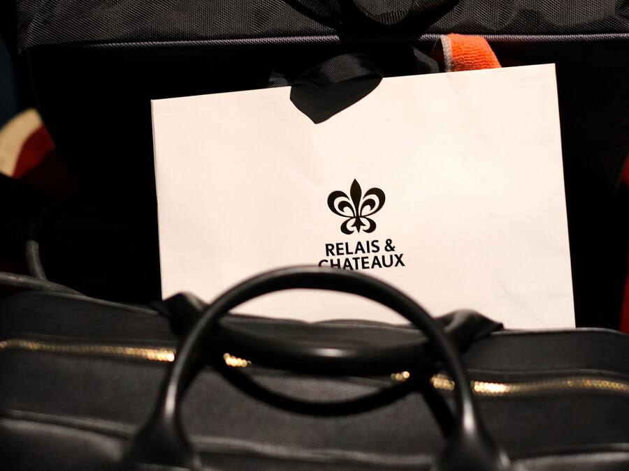 Een zwarte handtas met een witte label waarop 'RELAIS & CHATEAUX' staat.