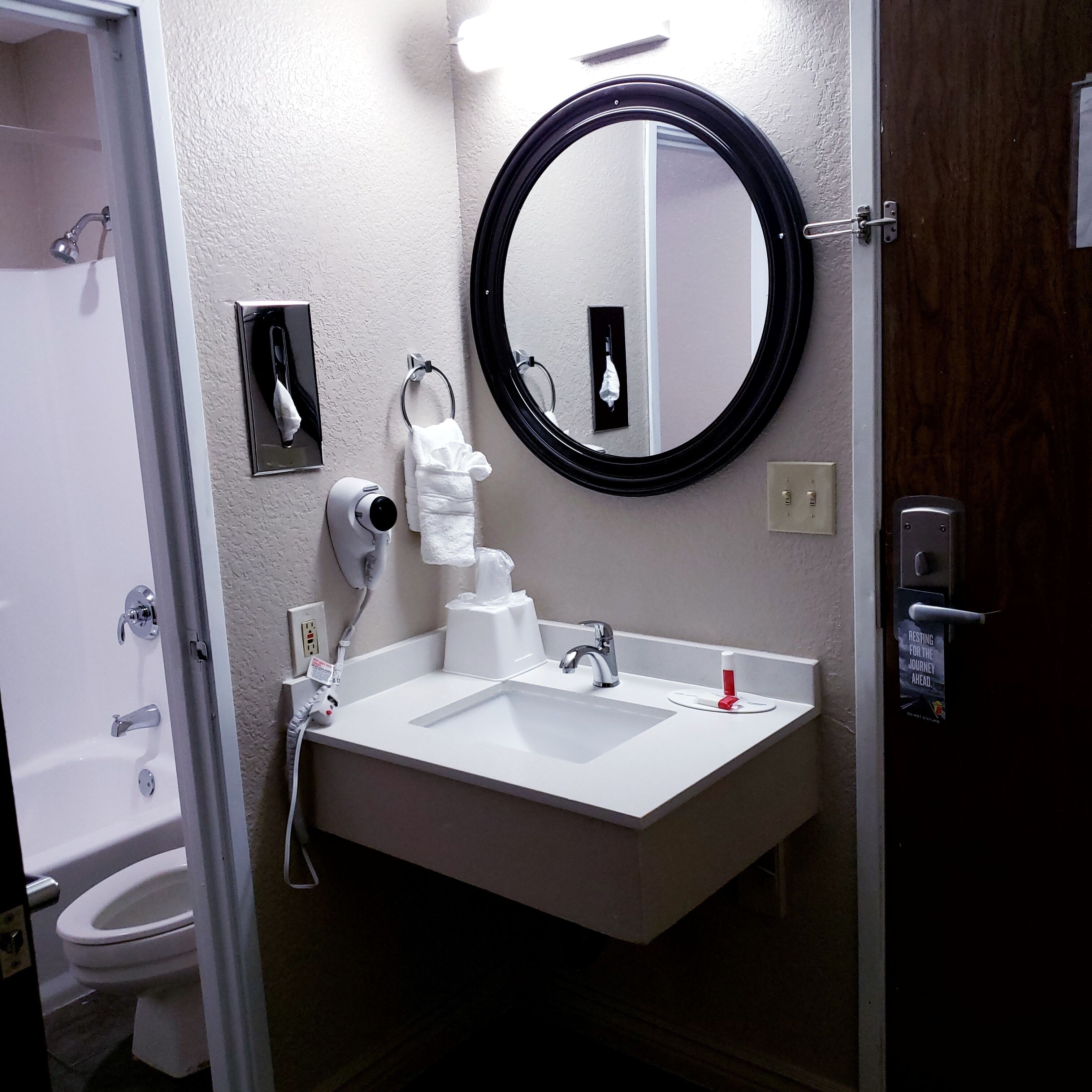 A bathroom with a white sink, a mirror, a towel dispenser, and a toilet.