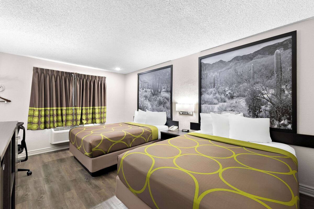 A hotel room with two beds, a desk, and a window with curtains.