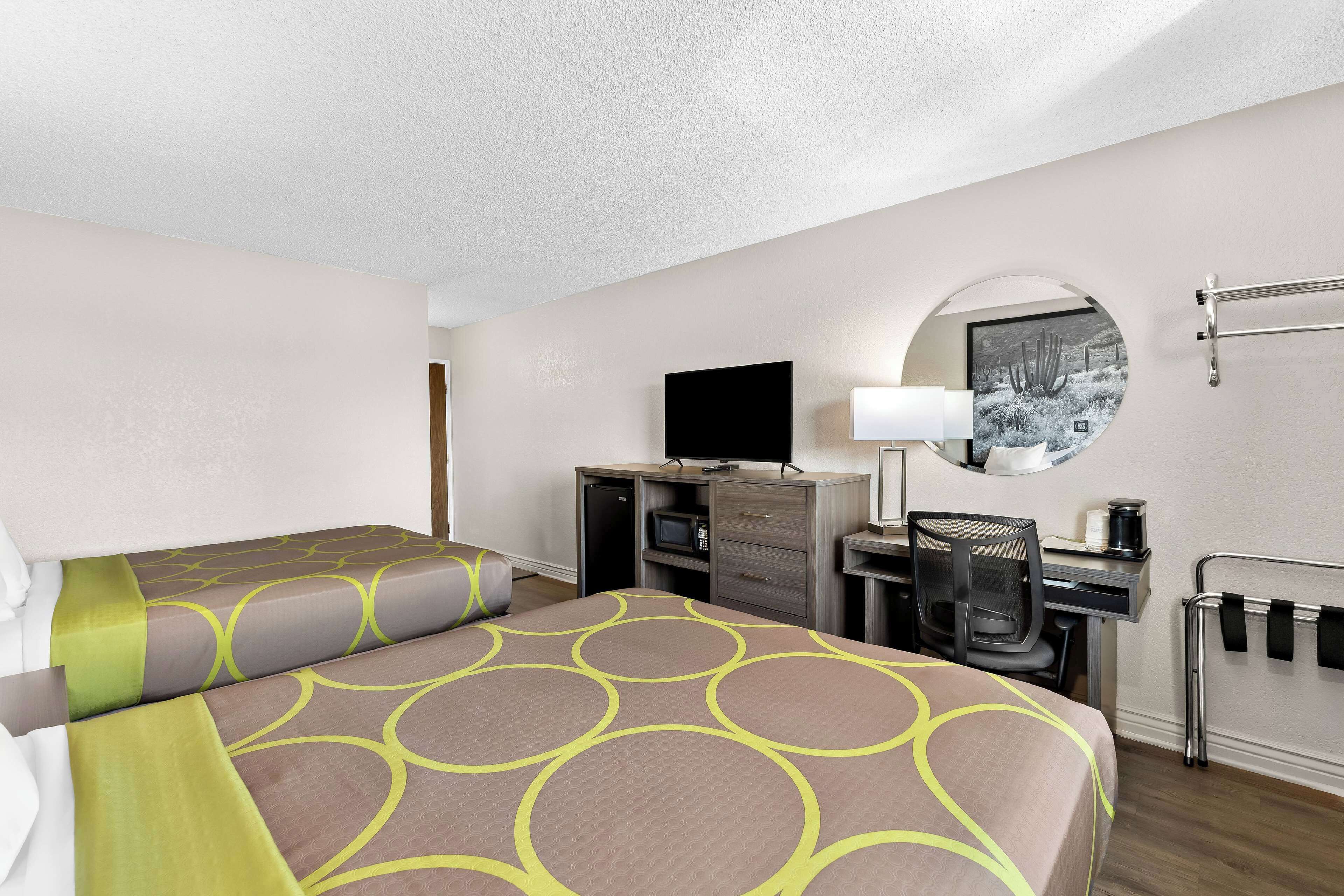 A hotel room with two beds, a desk, a chair, a TV, a mirror, and a radiator.