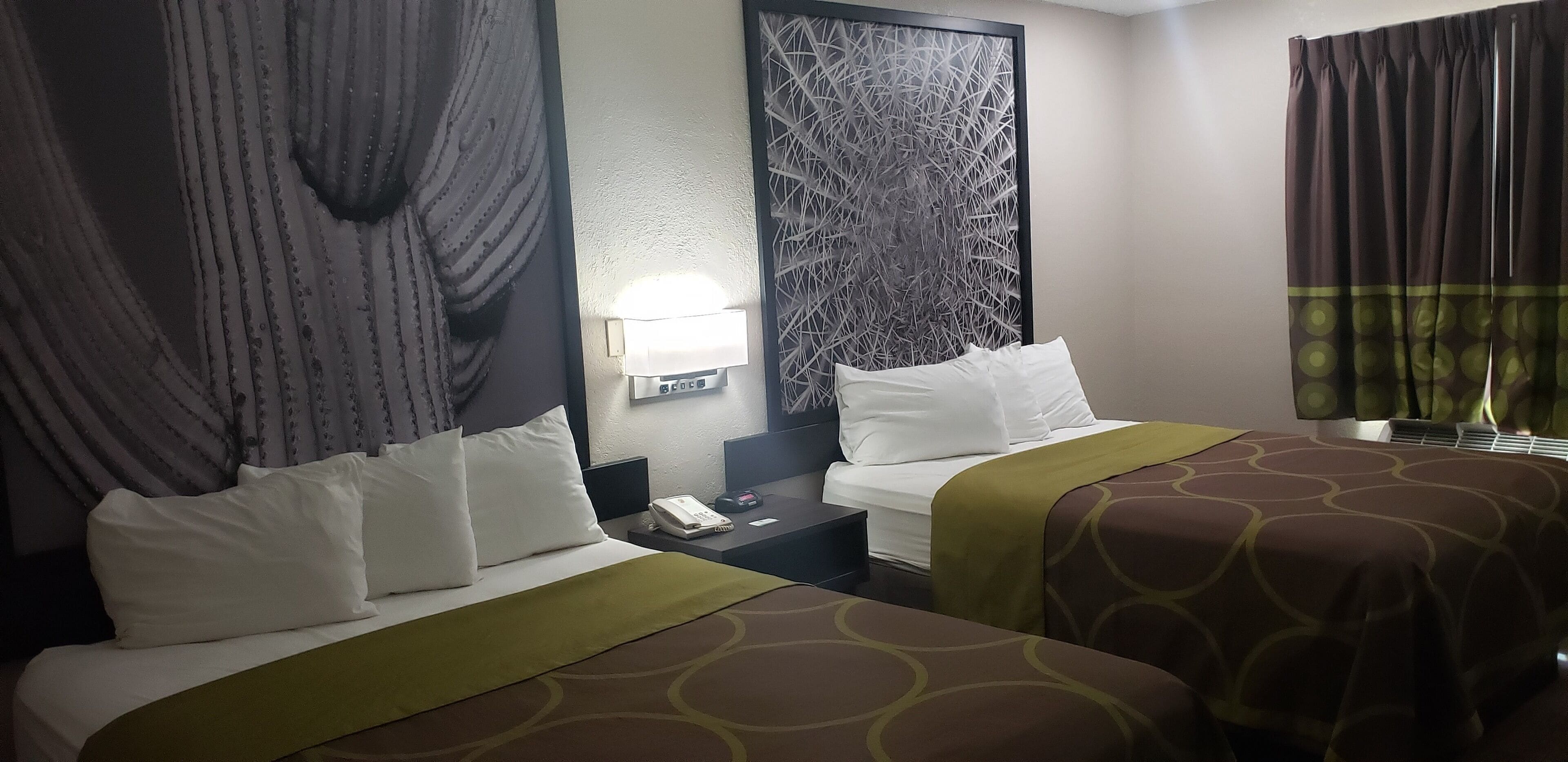 A hotel room with two beds, a nightstand, a lamp, and a patterned wall.