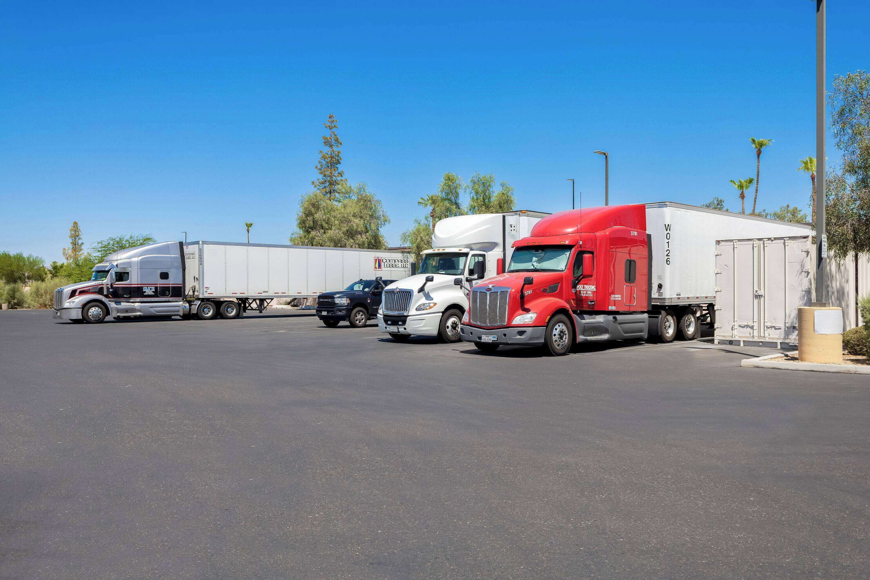 A parking lot with several trucks, including a red semi-truck and a white semi-truck.