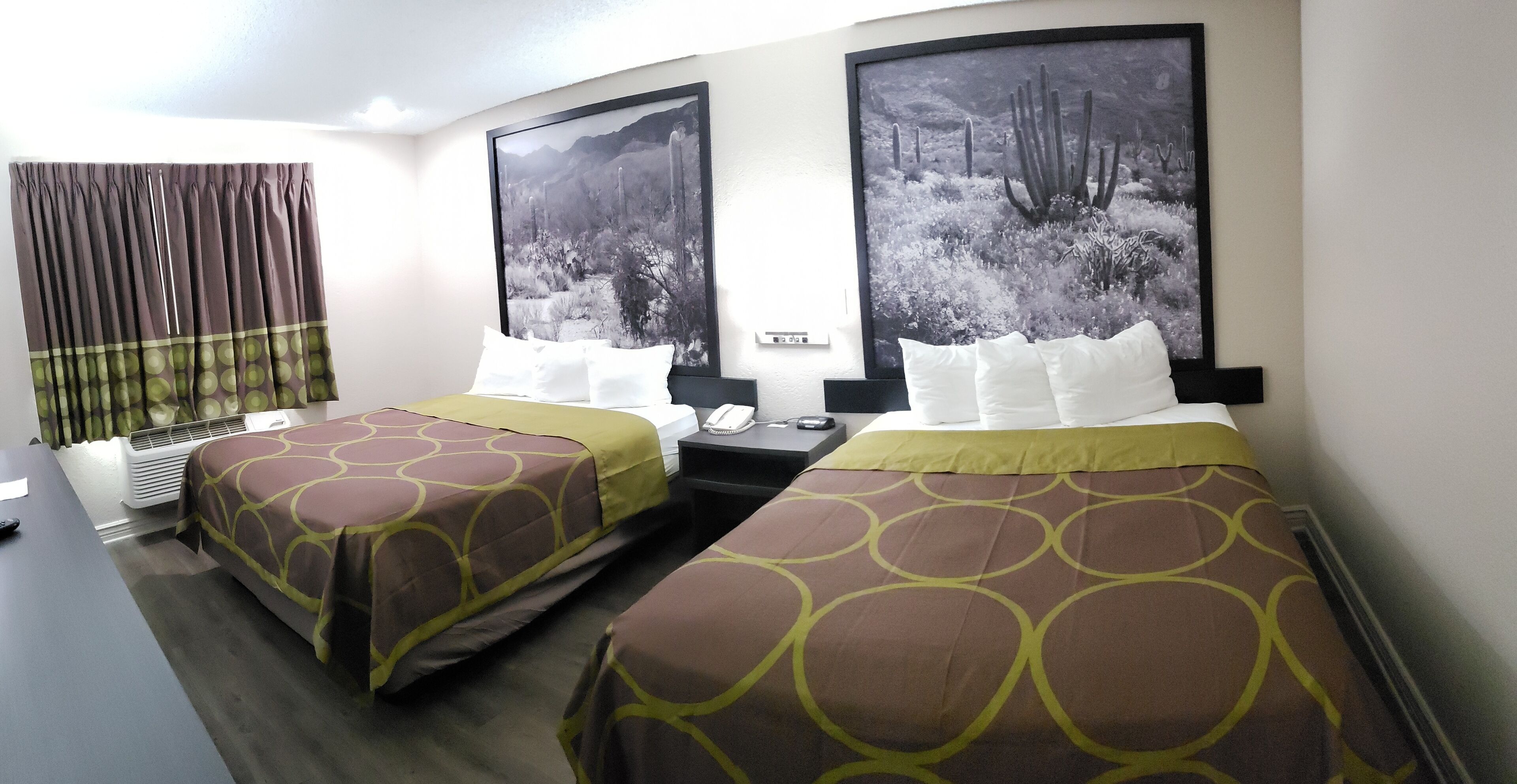 Une chambre d’hôtel avec deux lits, un bureau, un téléphone et une grande fenêtre avec des rideaux.
