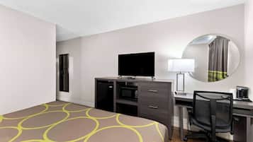 Ein Hotelzimmer mit einem Bett, einem Schreibtisch mit Computer, einem Sessel, einem Fernseher und einer Mikrowelle.