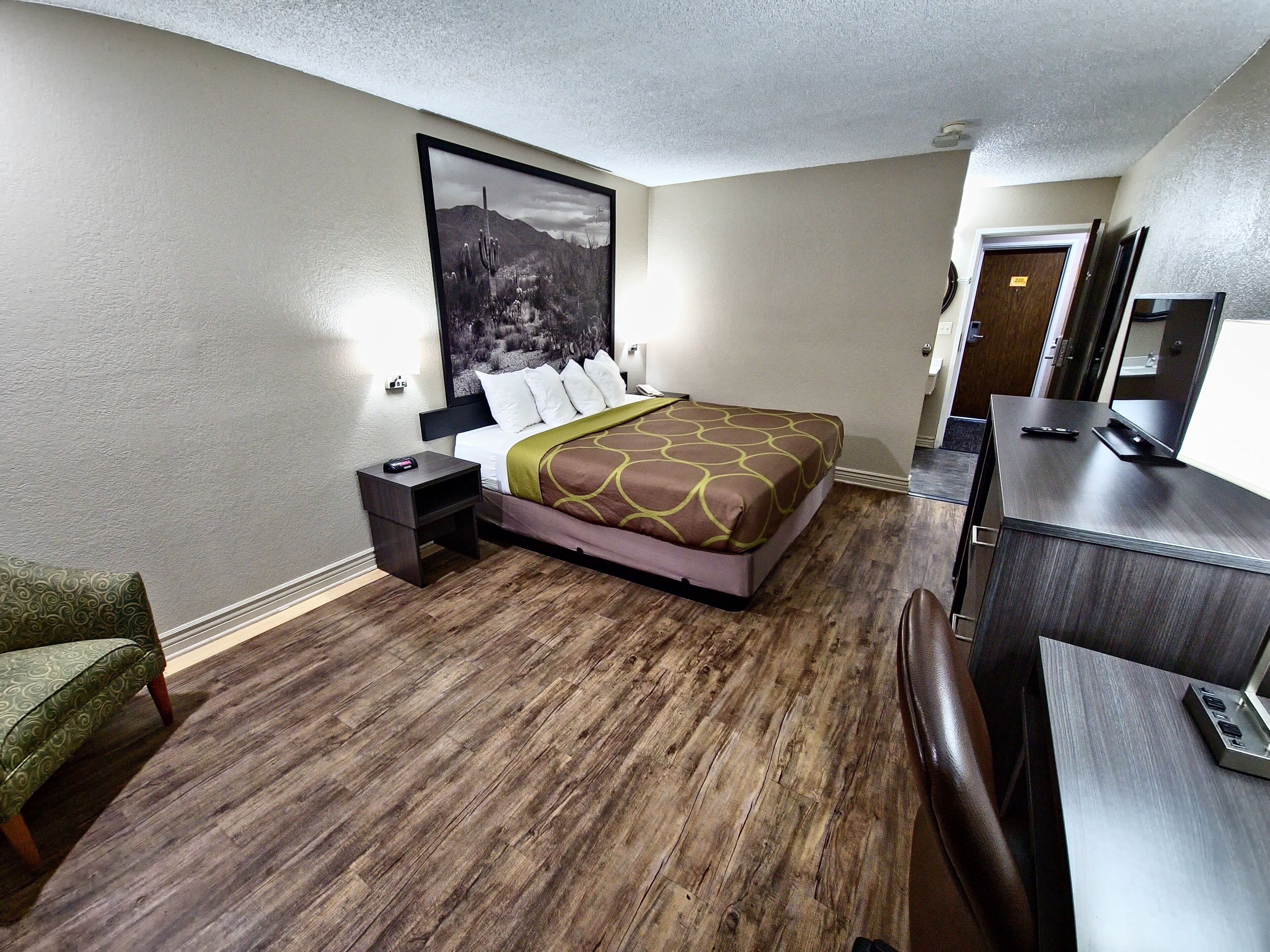 A hotel room with a bed, a nightstand, a desk, a chair, and a large framed picture on the wall.