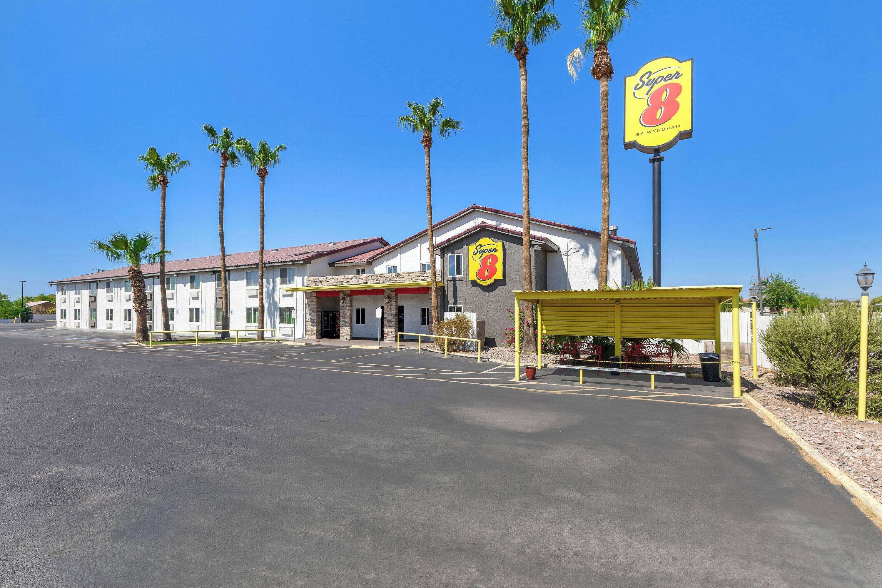 A Super 8 motel with a parking lot, palm trees, and a yellow covered area.