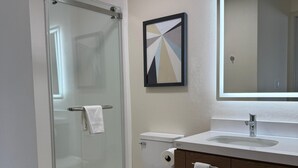Een moderne badkamer met een douchecabine van glas, een toilet, een wastafel met spiegel en een abstract kunstwerk in een lijst aan de muur.