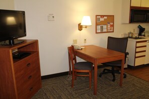Ein Hotelzimmer mit Holztisch, Stuhl, Fernseher, Lampe, Pinboard und einer Küchenzeile.