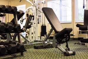Ein Fitnessstudio mit Trainingsgeräten, darunter Kurzhanteln, eine Bank und Kraftgeräte.