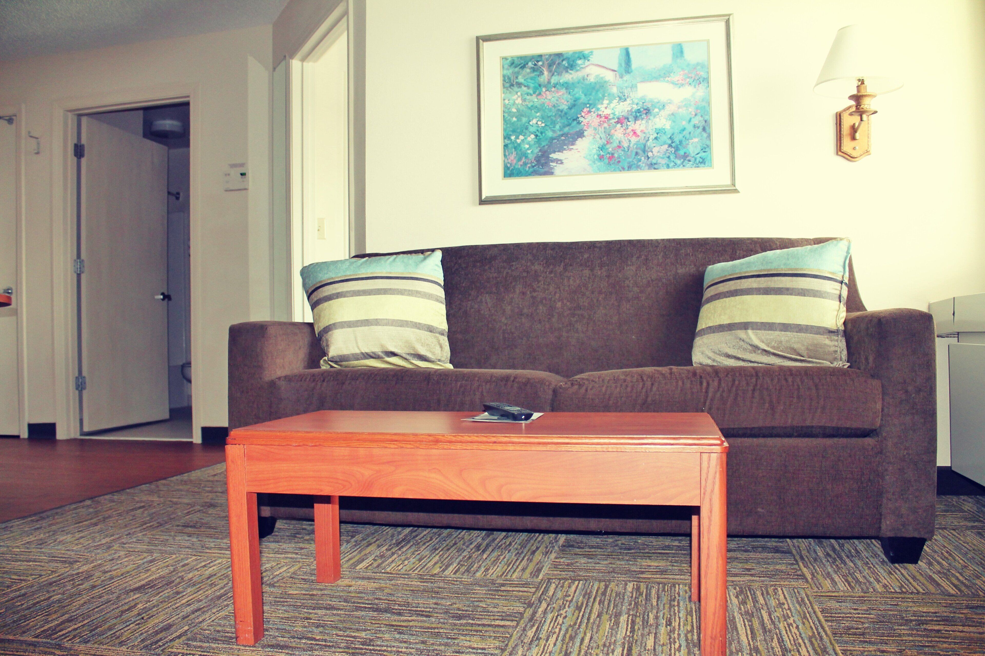 Una sala de estar con un sofá marrón, dos almohadas a rayas, una mesa de centro de madera y un cuadro en la pared.