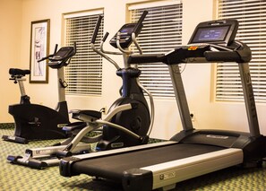 Un gimnasio con cintas de correr y bicicletas estáticas, que cuenta con pantallas digitales en los equipos.