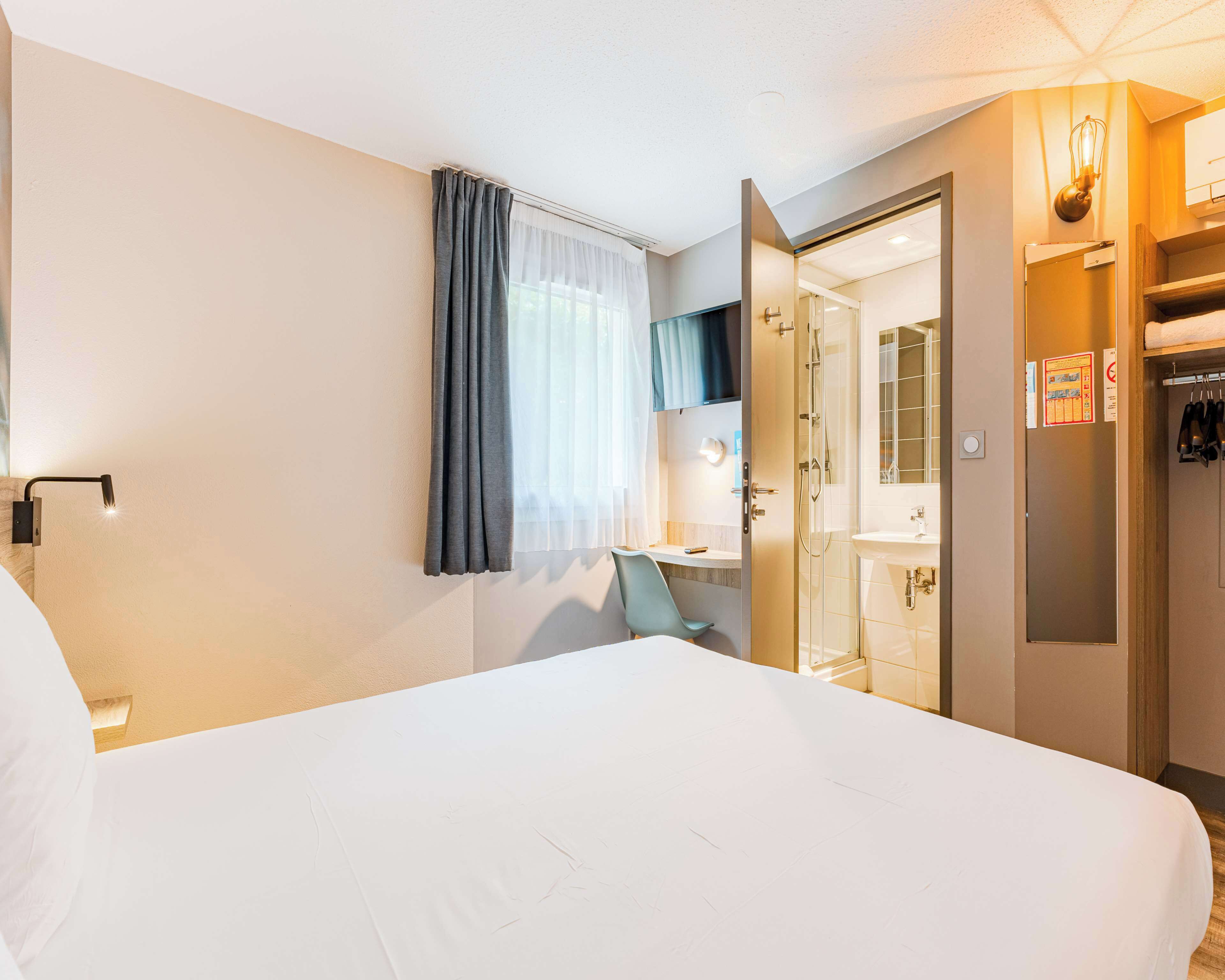 Une chambre d’hôtel comprenant un lit, une salle de bain avec douche, un miroir et une armoire.