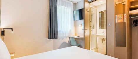 Ein Hotelzimmer mit Bett, Badezimmer mit Dusche, Spiegel und Kleiderschrank.