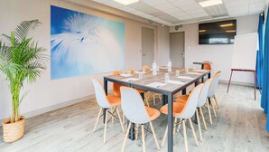 A conference room with a large table, chairs, a painting, a potted plant, and a TV screen. - KYRIAD DIRECT Tours Sud - Chambray Lès Tours (Chambray-les-Tours)