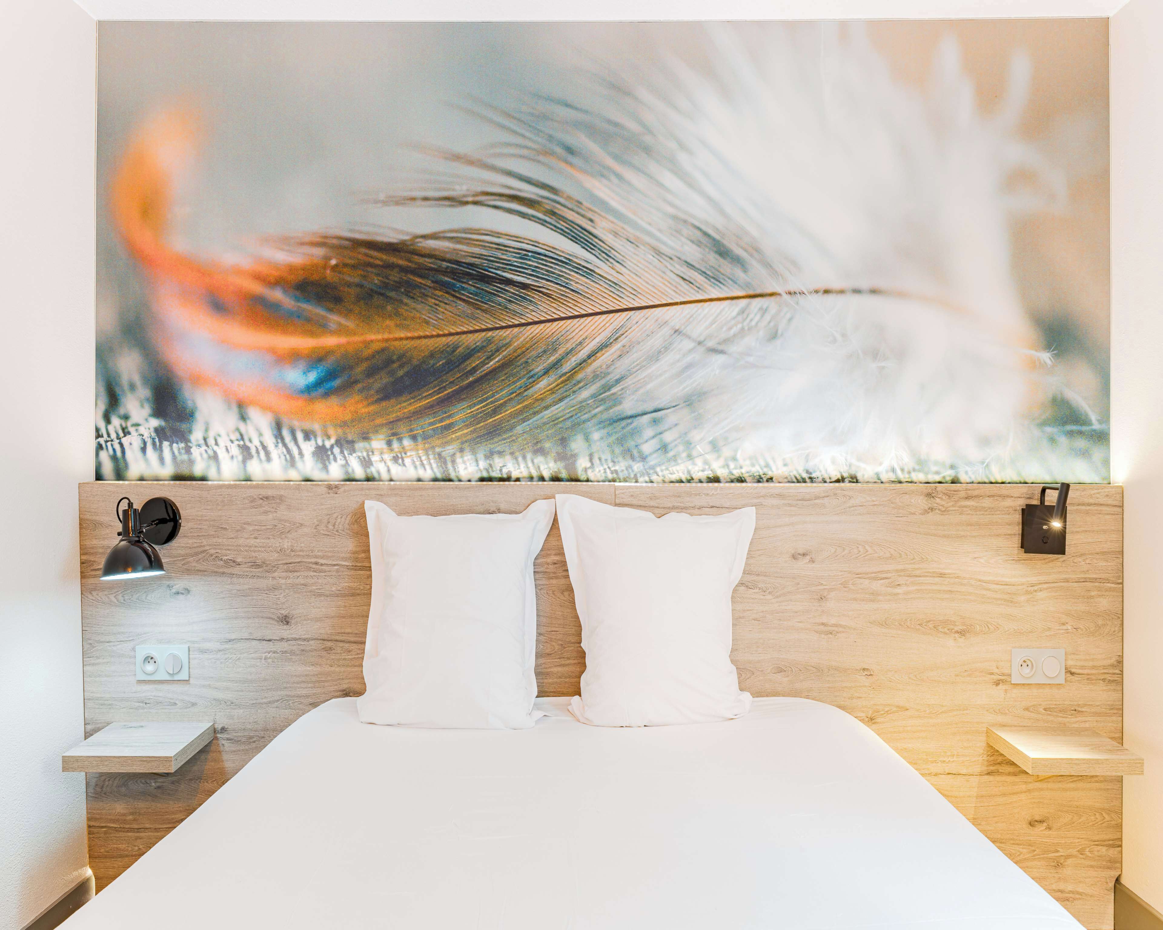 A neatly made bed with two pillows, a wall-mounted nightstand with a lamp, and a large abstract painting above the bed.