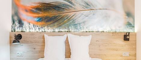 A neatly made bed with two pillows, a wall-mounted nightstand with a lamp, and a large abstract painting above the bed.