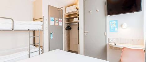 A hotel room with a bunk bed, a desk with a chair, a TV mounted on the wall, and a closet with a mirror.