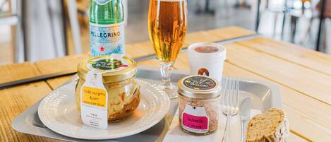 Een dienblad met een flesje Pellegrino water, een glas bier, een potje saus, een potje chocoladepasta en een sneetje brood op een houten tafel in een restaurant.