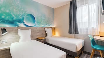 Habitación de hotel con dos camas, cabecero de madera, un mural en la pared, ventana con cortinas, escritorio con silla y un cubo de basura.