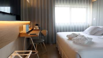 Una habitación de hotel con cama, escritorio, silla, televisor y ventana con cortinas.