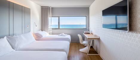 Habitación de hotel con dos camas, un escritorio, una silla, un televisor y un ventanal con vistas al mar.