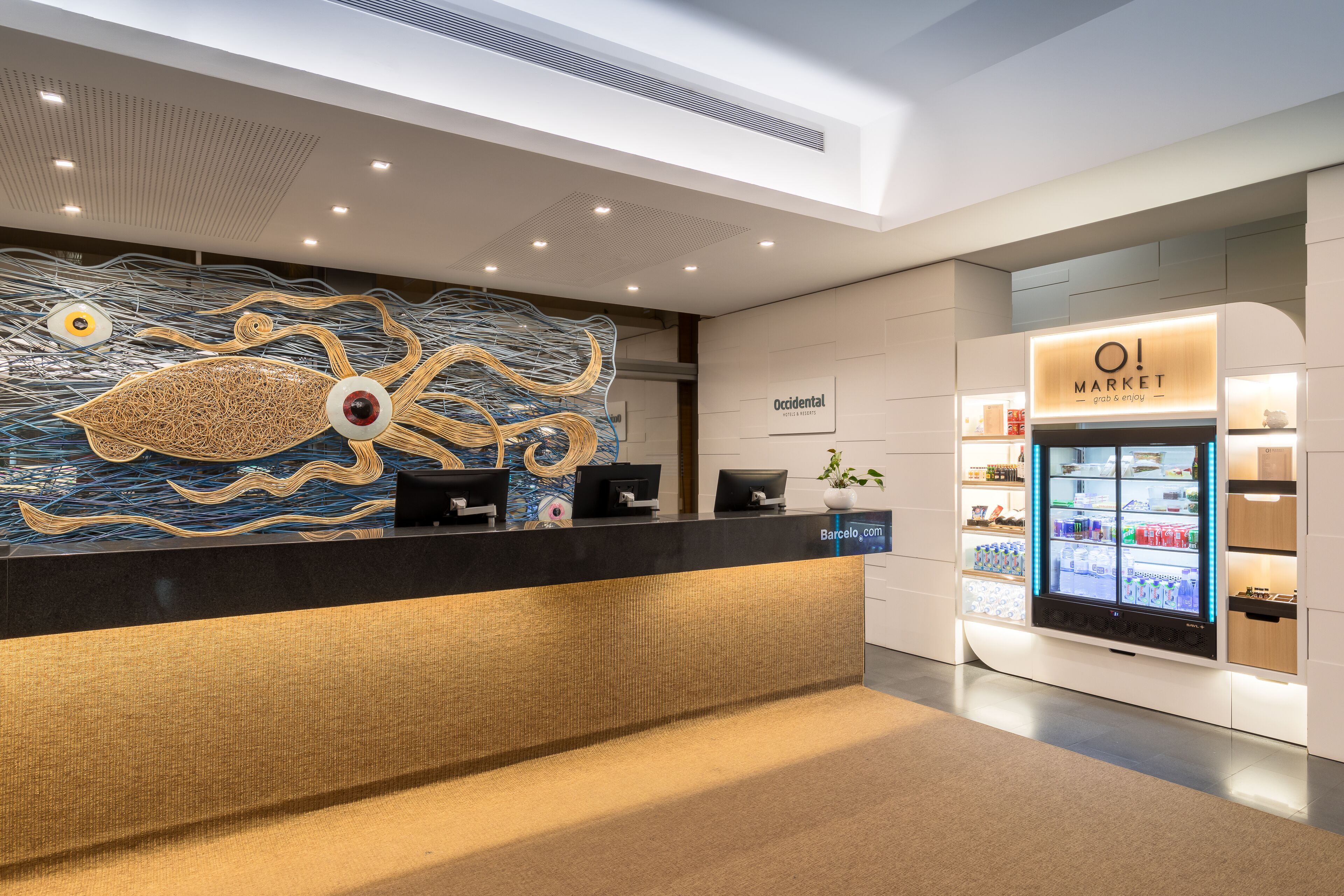 A modern reception area with a unique wall art, a digital kiosk, and a refrigerated display case.