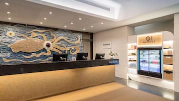 A modern reception area with a unique wall art, a digital kiosk, and a refrigerated display case.