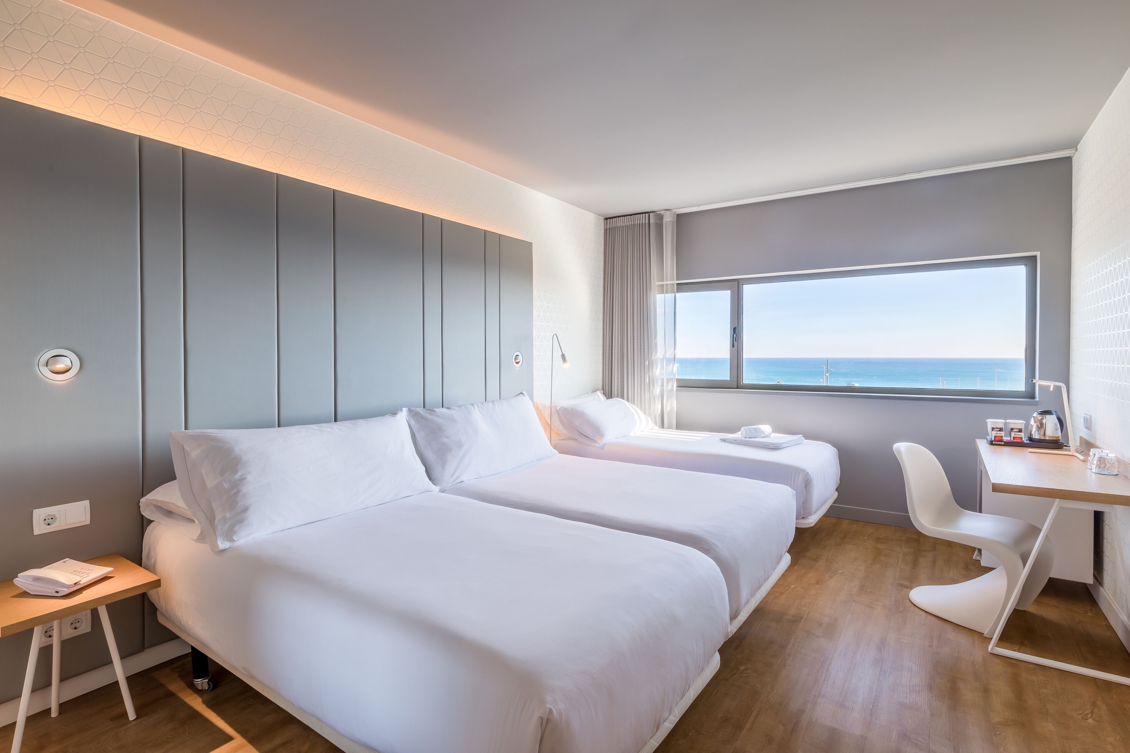 Une chambre d’hôtel avec deux lits, un bureau et vue sur la mer.