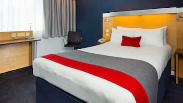 Una habitación de hotel con una cama grande, un escritorio, una silla y una mesita de noche con una lámpara.