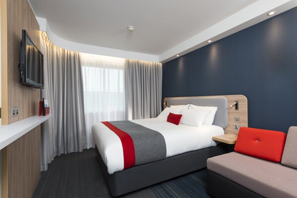 A modern hotel room with a large bed, a flat-screen TV mounted on the wall, a bedside table, and a red upholstered chair. - Holiday Inn Express Cambridge by IHG (Cambridge)
