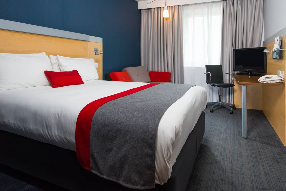 A hotel room with a large bed, a desk with a computer and phone, and a TV.