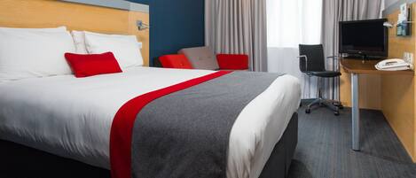Une chambre d’hôtel avec un grand lit, un bureau équipé d’un ordinateur et d’un téléphone, et une télévision.