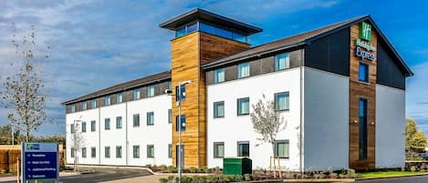 A Holiday Inn Express hotel with a modern design, featuring a mix of white and wooden facades, large windows, and a landscaped entrance area.