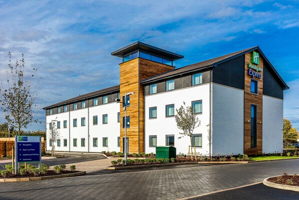 A Holiday Inn Express hotel with a modern design, featuring a mix of white and wooden facades, large windows, and a landscaped entrance area.