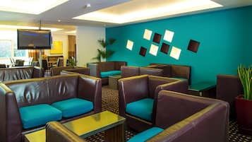 A hotel lobby with leather seating, a flat-screen TV, and a wall with square light fixtures.