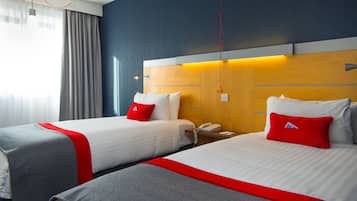 A hotel room with two beds, each with a red pillow, a wooden headboard, and a bedside table with a phone.
