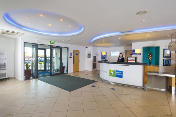A hotel reception area with a modern design, including a reception desk, a waiting area, and a glass door entrance. - Holiday Inn Express Cambridge by IHG (Cambridge)