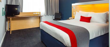 Een hotelkamer met een bed, een bureau met televisie, een stoel en een raam met gordijnen.