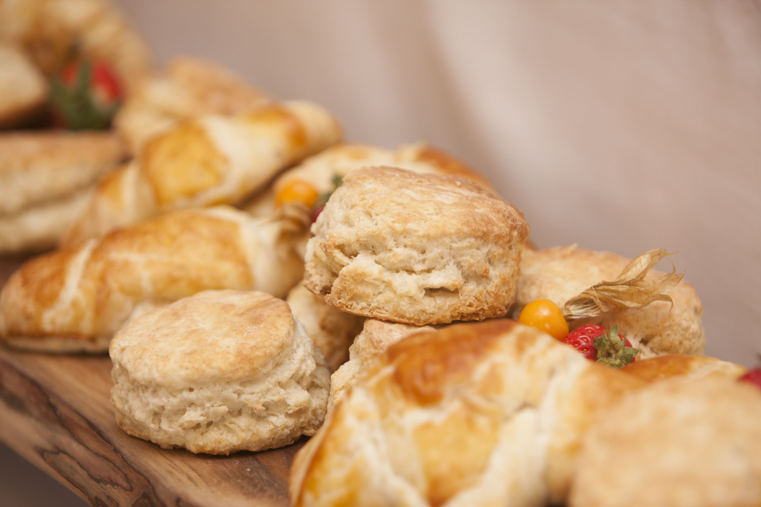 A wooden board with several pastries, including biscuits and a small fruit garnish.