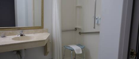 A bathroom with a sink, mirror, shower, and a small stool.
