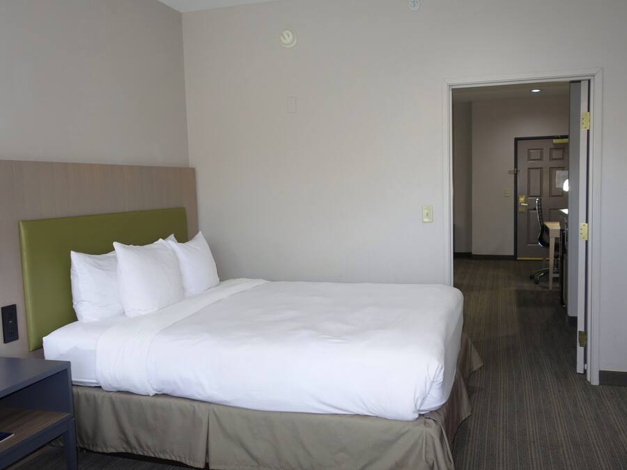 Quarto de hotel com uma cama grande, cabeceira verde e porta para um banheiro.