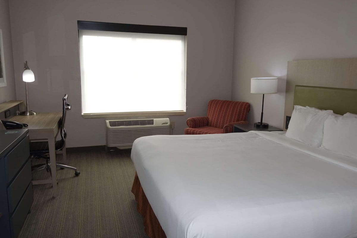 Una habitación de hotel con una cama grande, un escritorio con lámpara, una silla y una ventana con persianas.