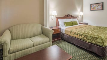 Habitación de hotel con un sofá de color verde con estampado, una mesita de noche de madera, una cama con edredón verde estampado y una alfombra verde estampada.