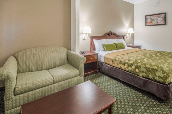 A hotel room with a green patterned sofa, a wooden nightstand, a bed with a green patterned bedspread, and a green patterned carpet. - Econo Lodge Weatherford (Weatherford)