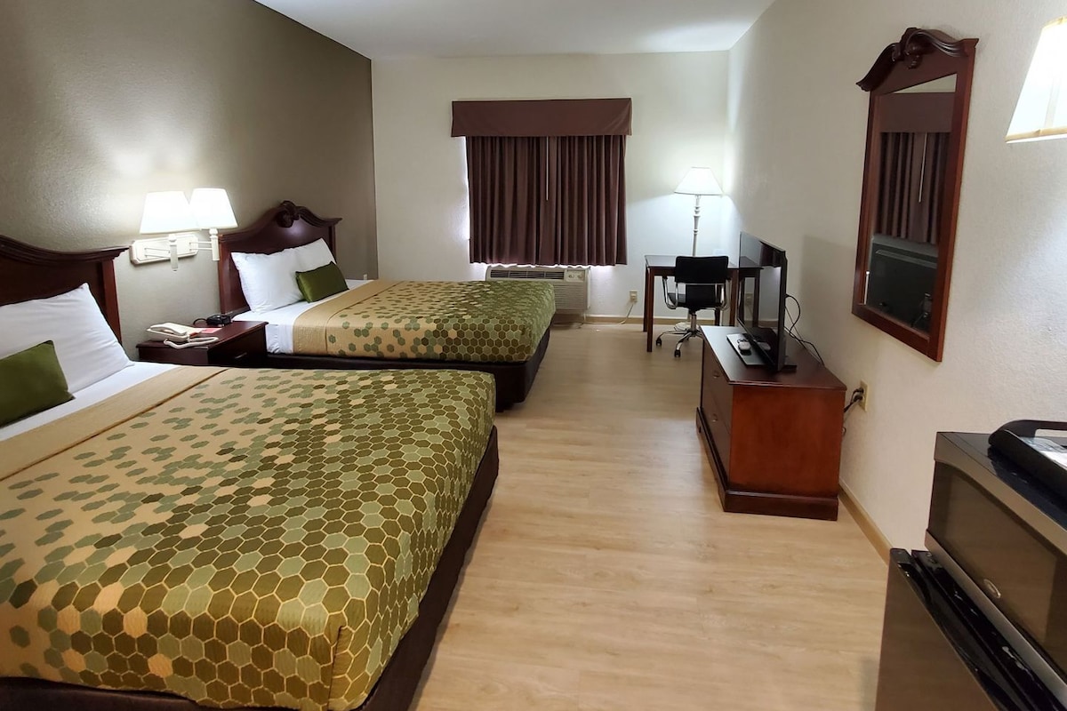 A hotel room with two beds, a desk, a chair, a TV, and a mirror.
