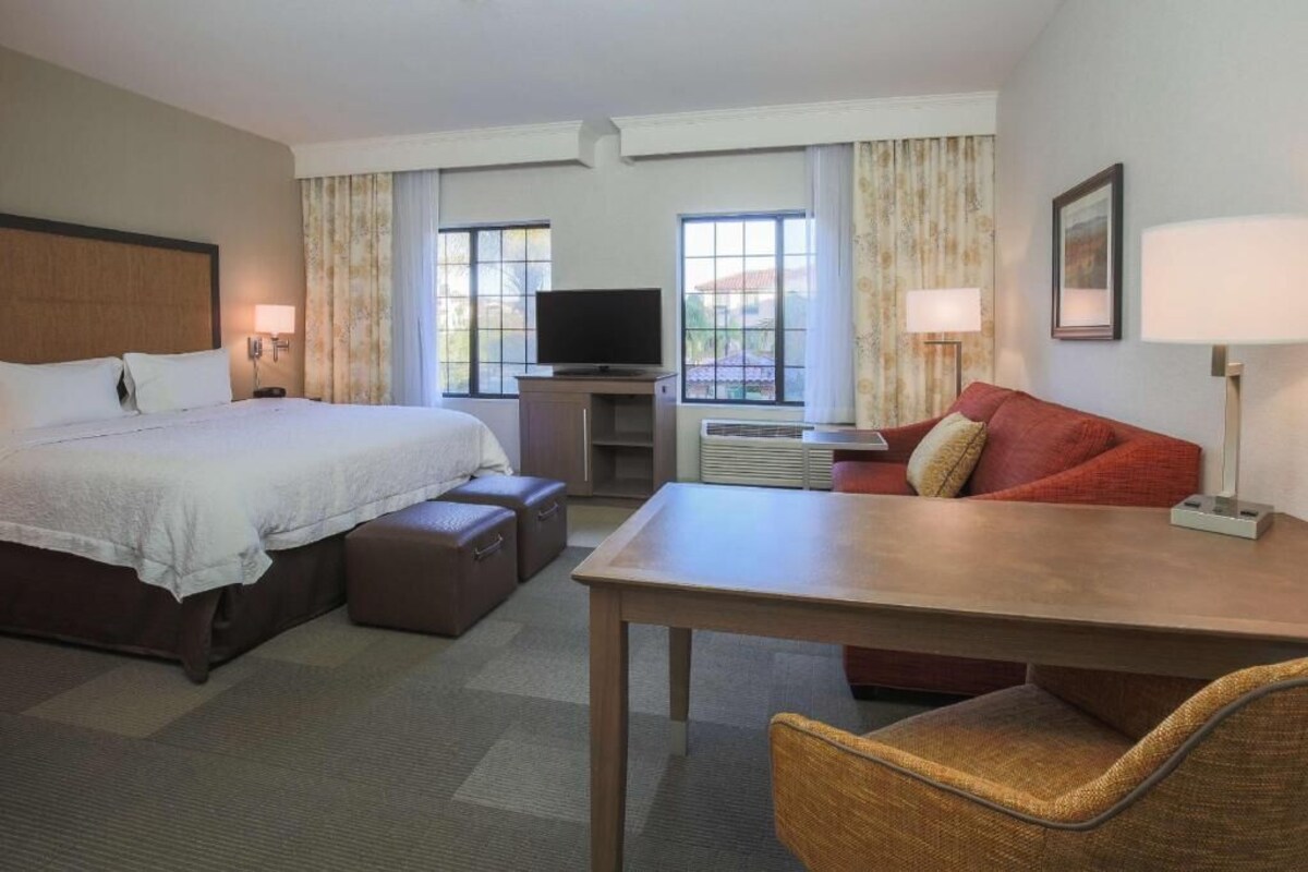 A hotel room with a bed, a TV, a table, a sofa, and a chair.