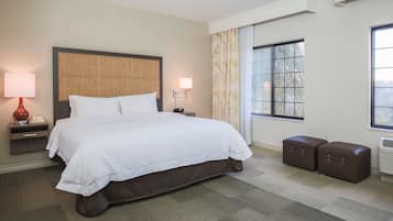 Una habitación de hotel con una cama grande, lámparas de noche, una ventana con cortinas y un radiador.