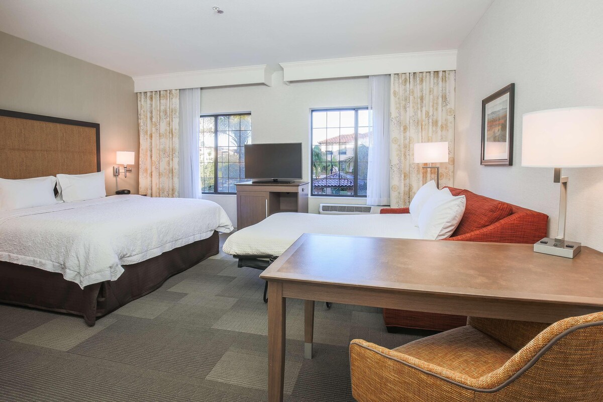 A hotel room with two beds, a TV, a desk, and a chair.