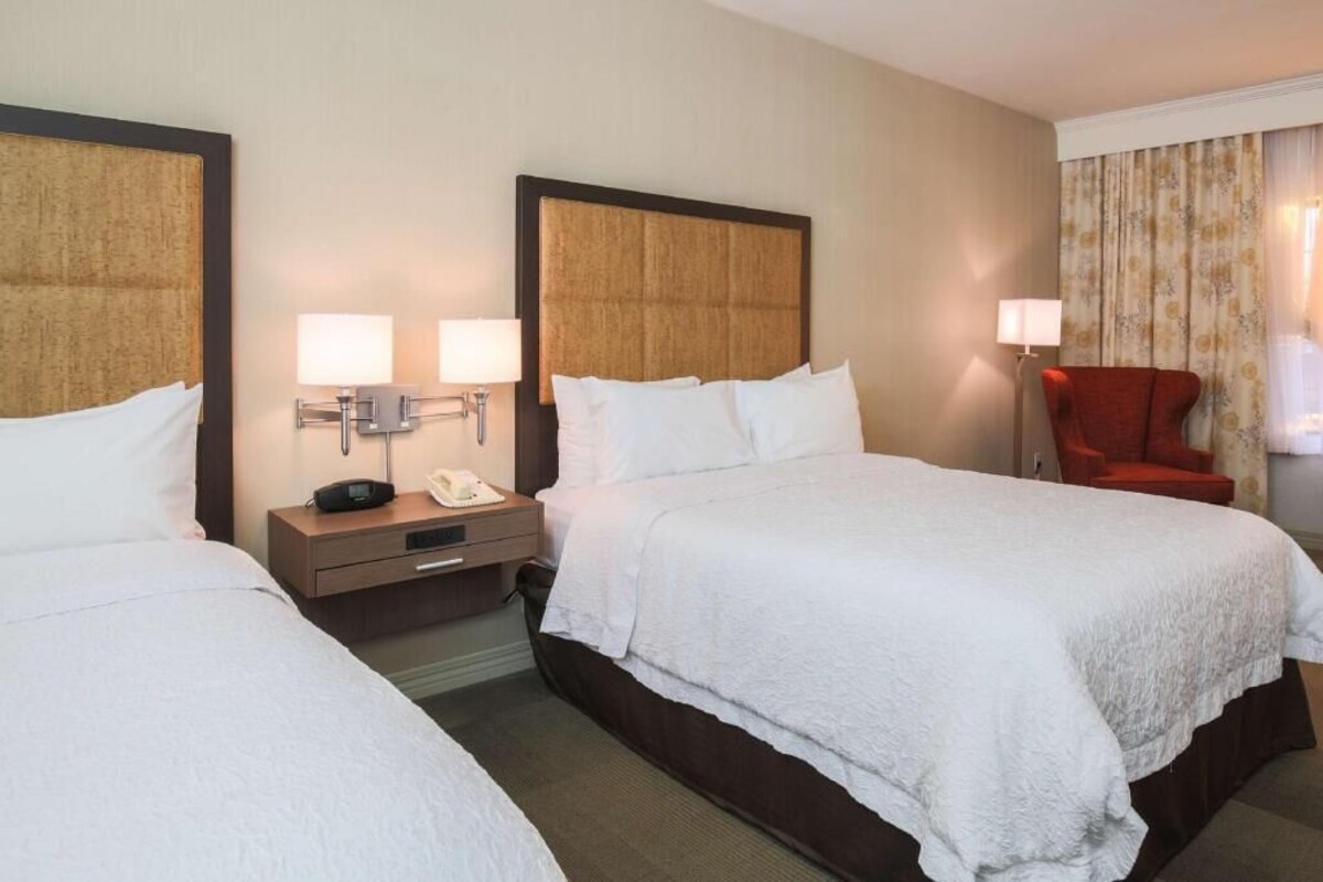 A hotel room with two beds, bedside tables with lamps, a red chair, and a telephone.