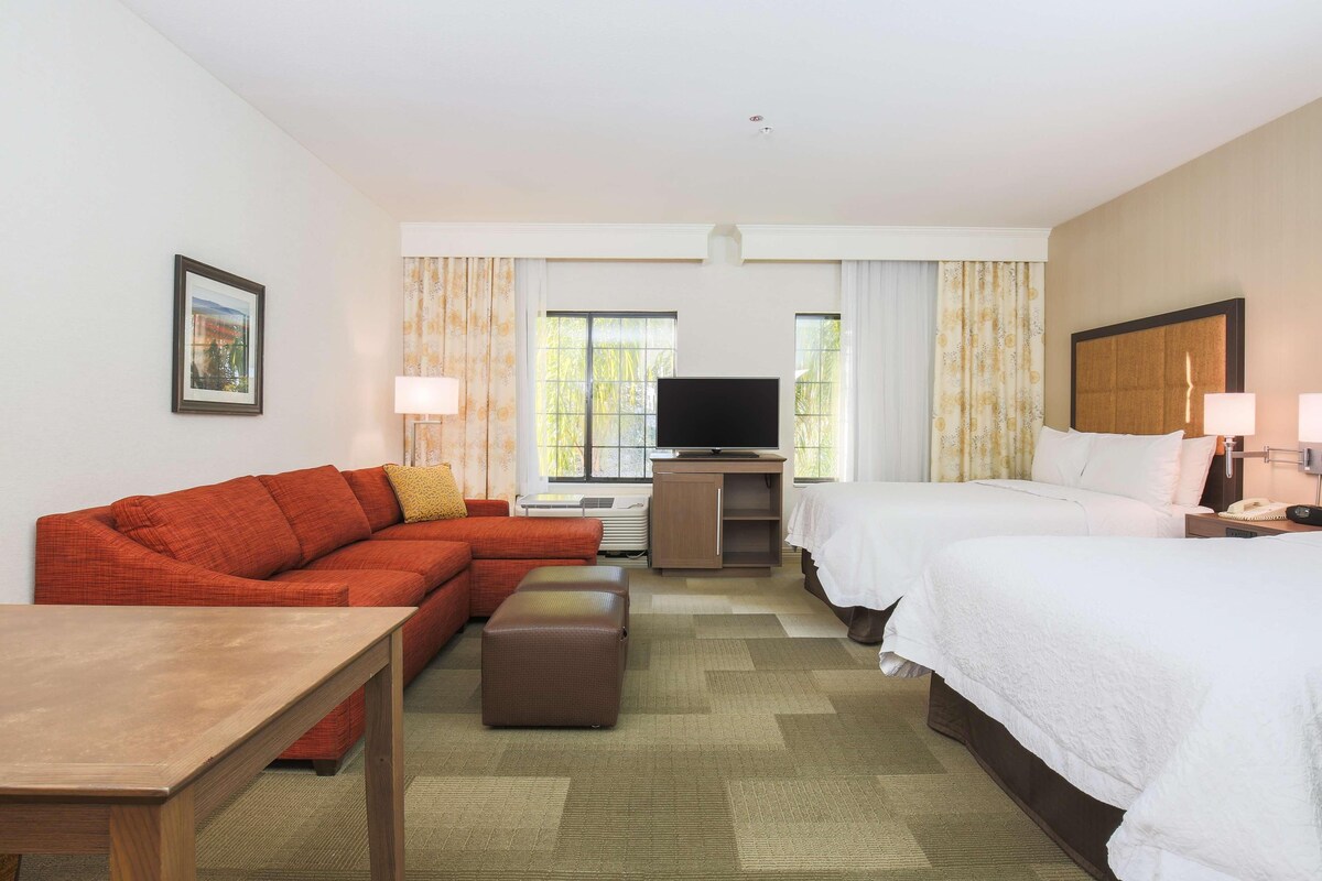 A hotel room with a sofa, two beds, a TV, and a desk.